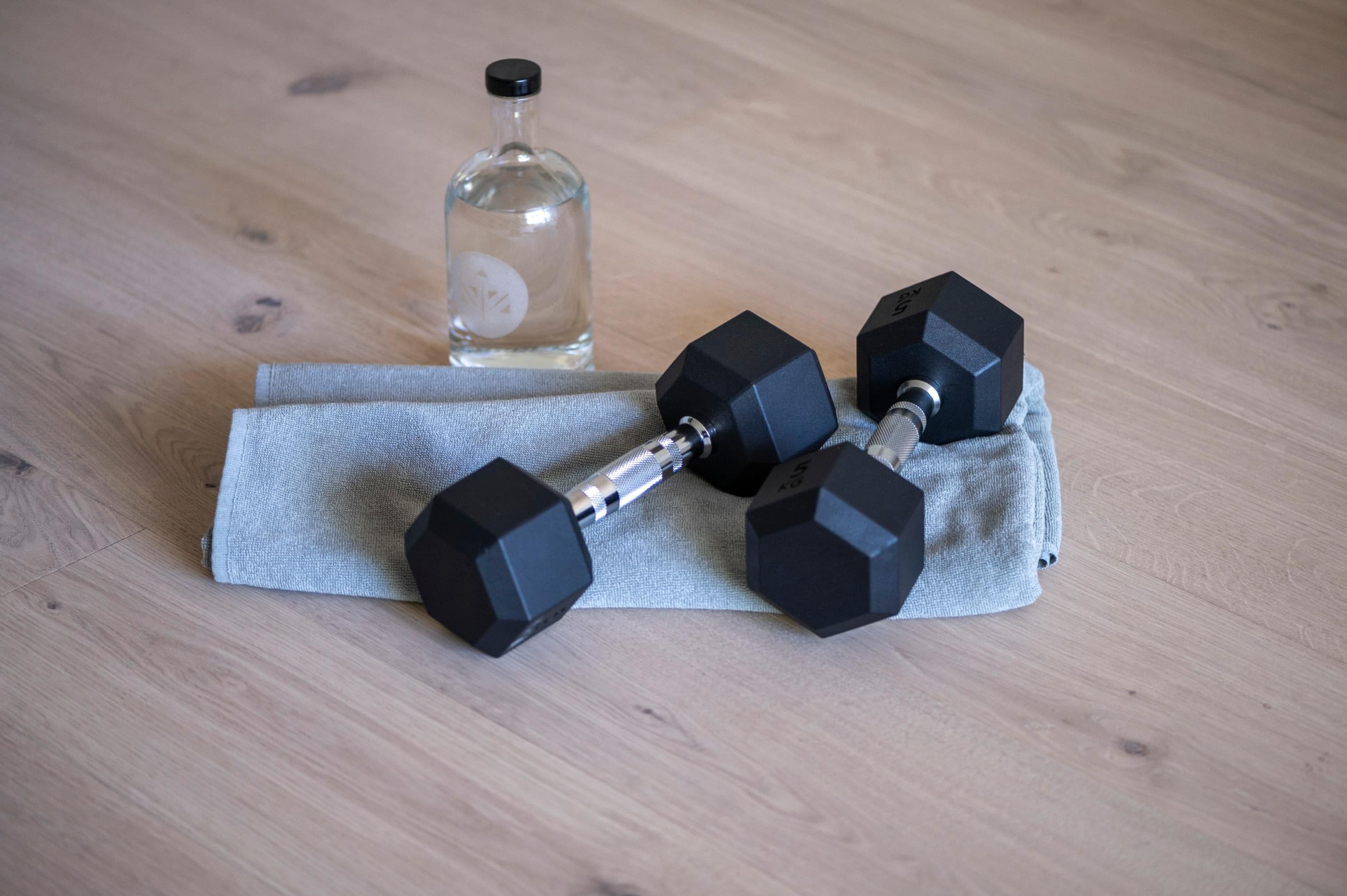 A pair of black hexagonal dumbbells on a grey towel on a wooden floor.