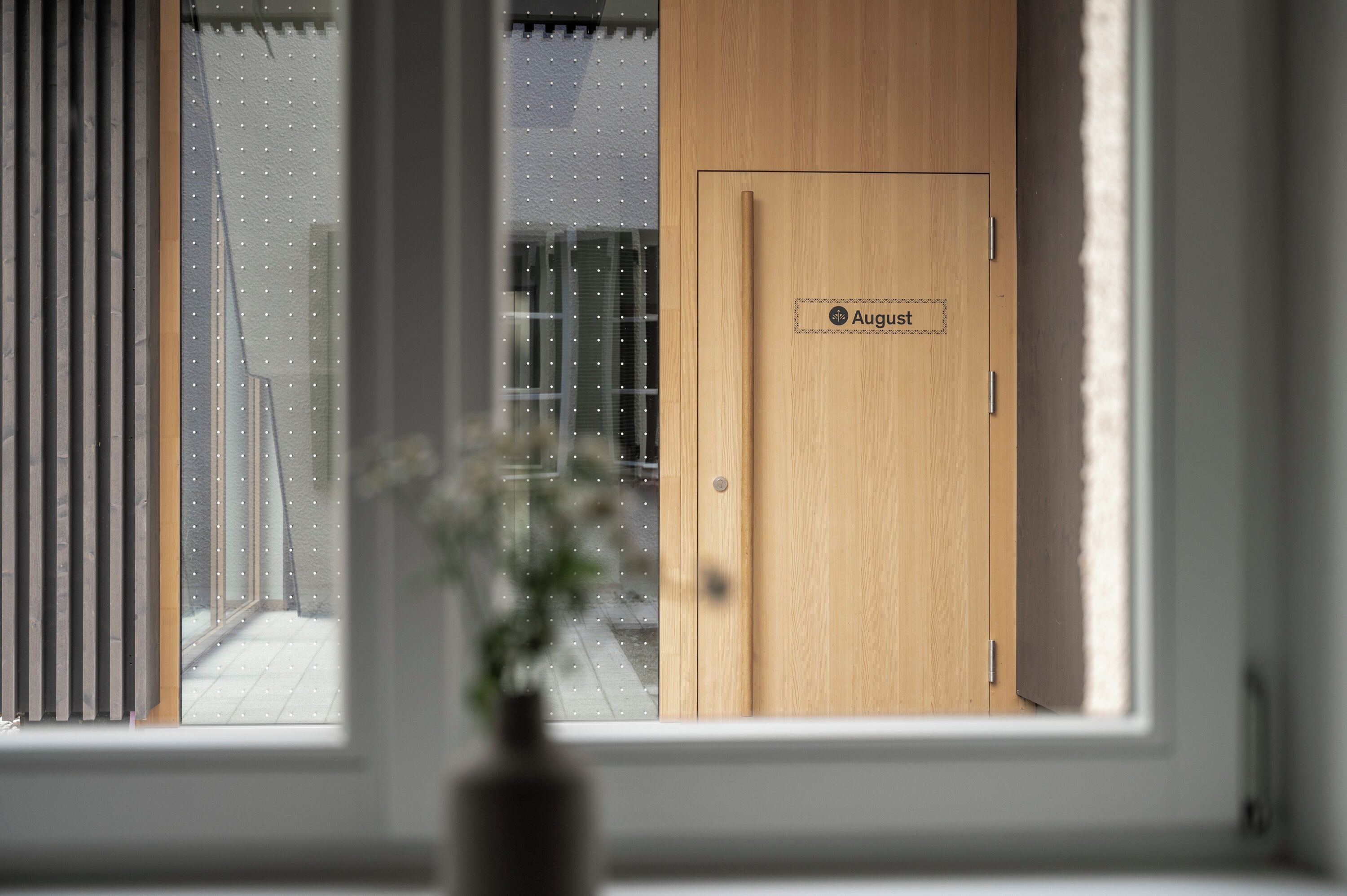 Eine Holzt ür mit dem Aufkleber 'August' und ein Fenster mit Jalousien.