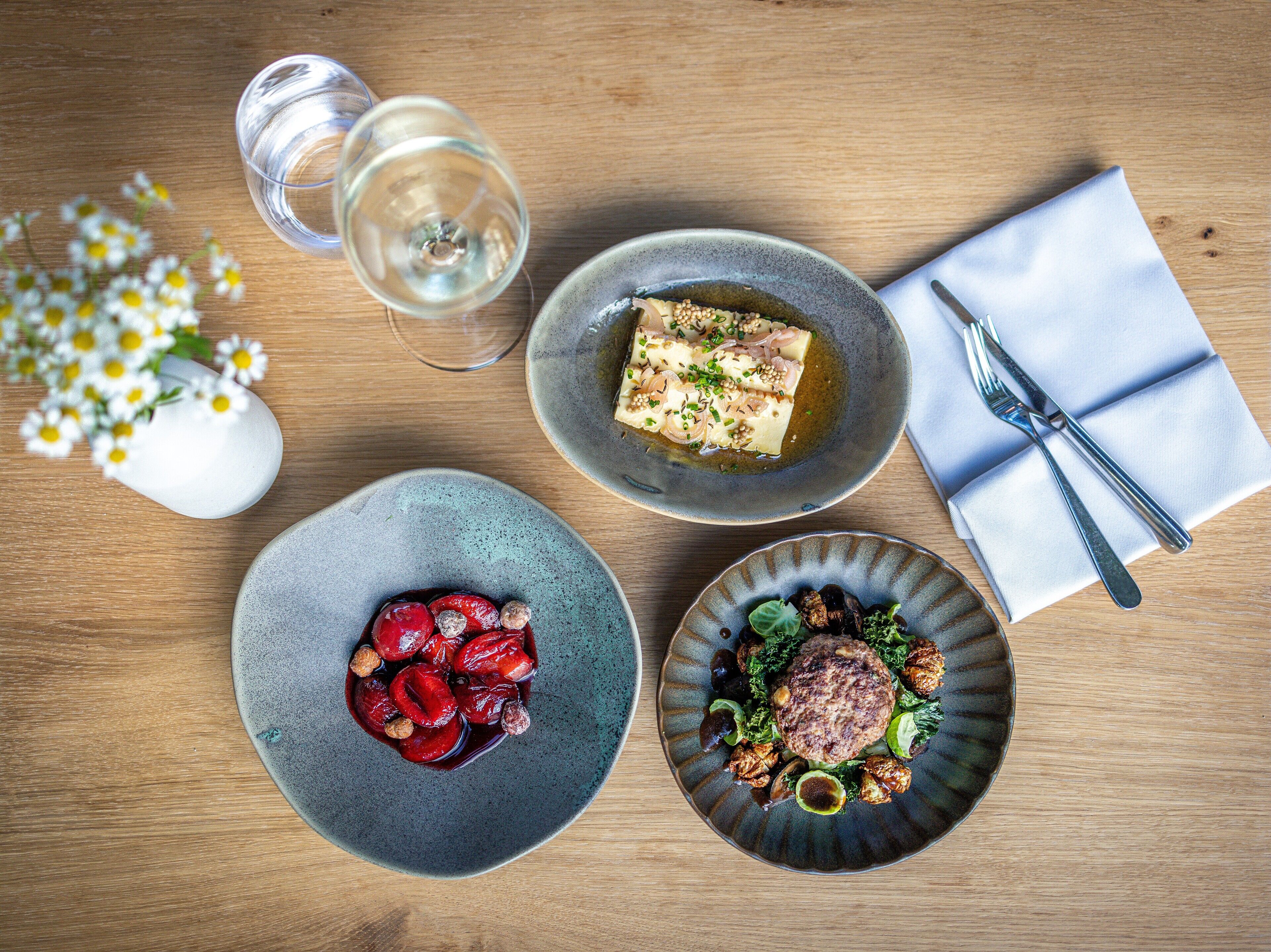 Una mesa de madera con tres platos, un vaso de agua y un jarrón con flores.
