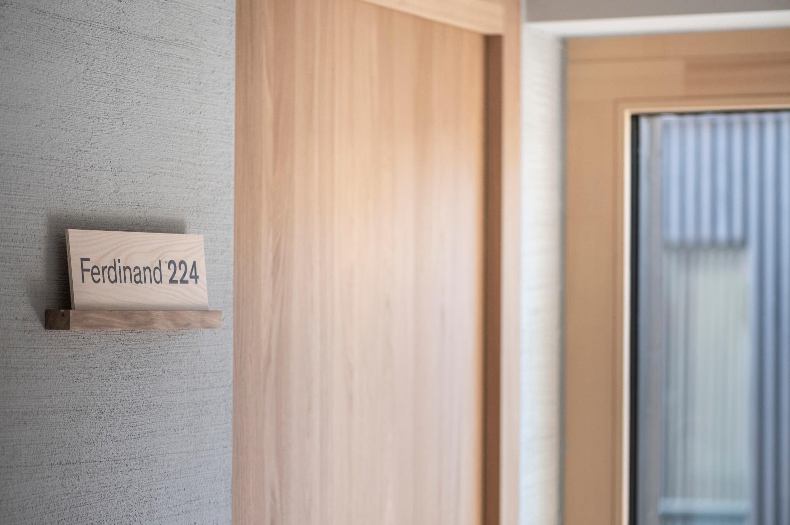A wooden nameplate with 'Ferdinand 224' on a textured wall.