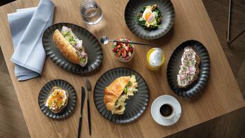 Une table en bois sur laquelle on trouve différents plats, notamment des sandwichs, une salade et une tasse de café.