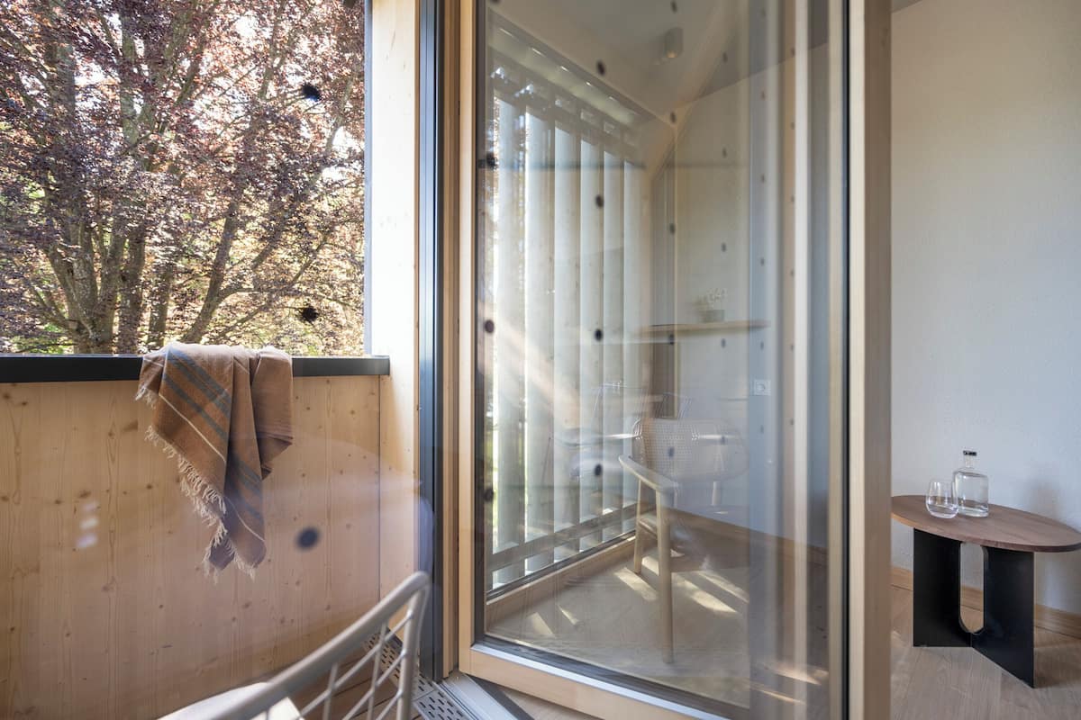 A modern room with a large sliding glass door leading to a balcony, a small wooden table with a glass container, and a towel hanging on the railing.