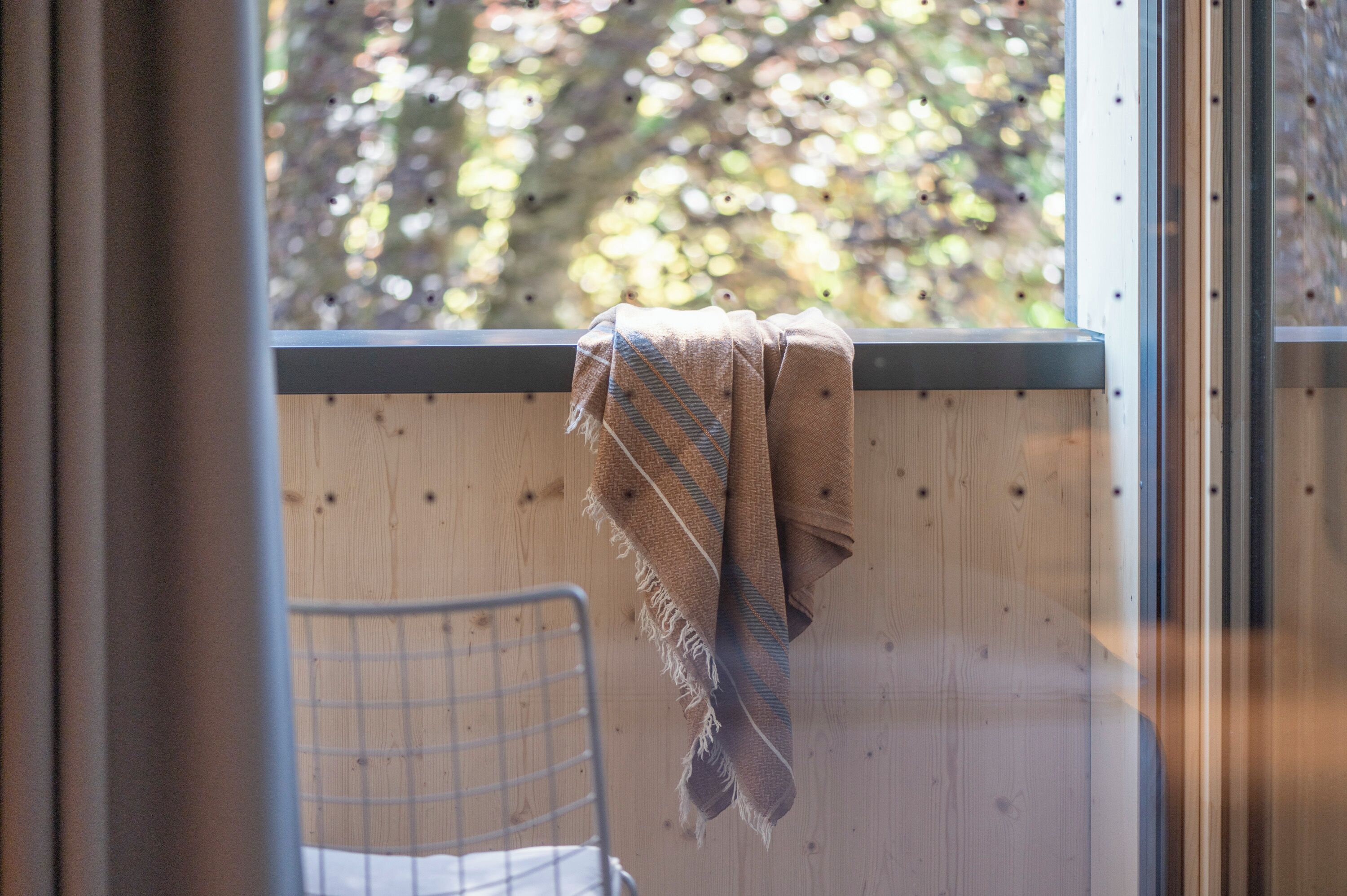 Une pièce avec un mur en bois, une fenêtre donnant sur des arbres et une chaise en métal.