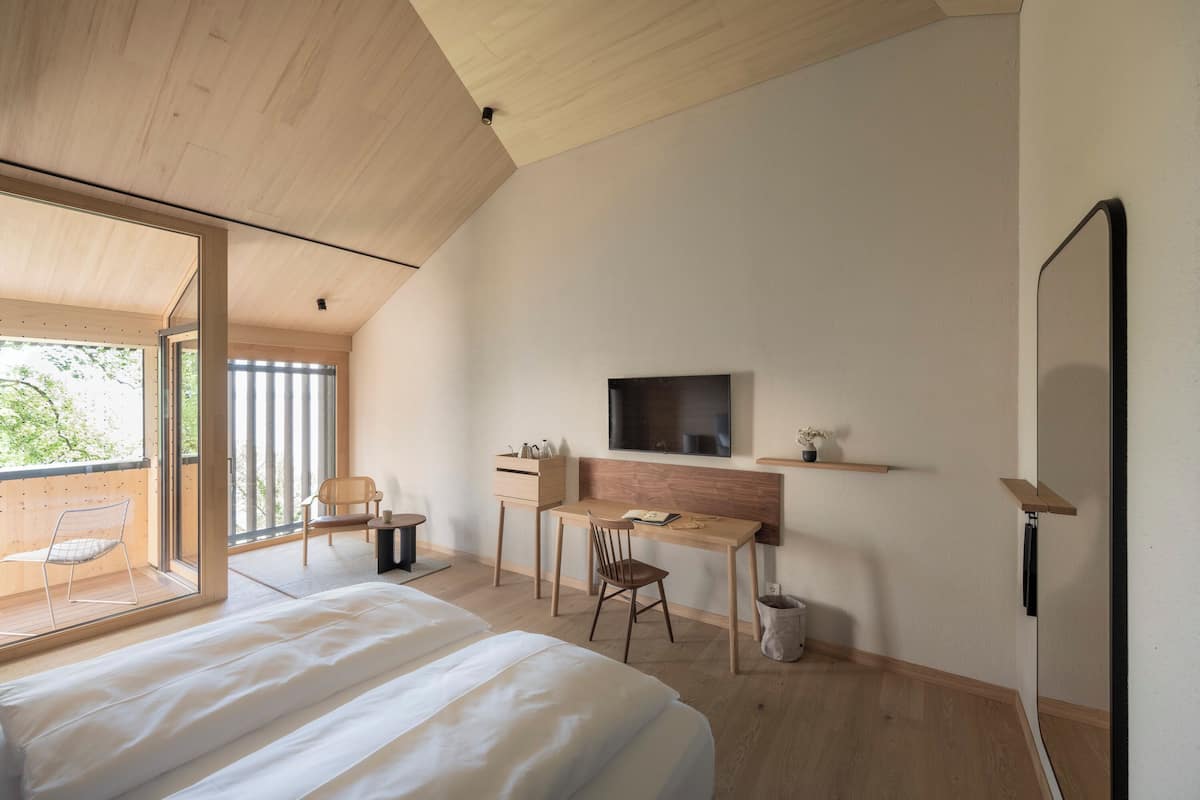 A modern bedroom with a large bed, a desk, and a TV.