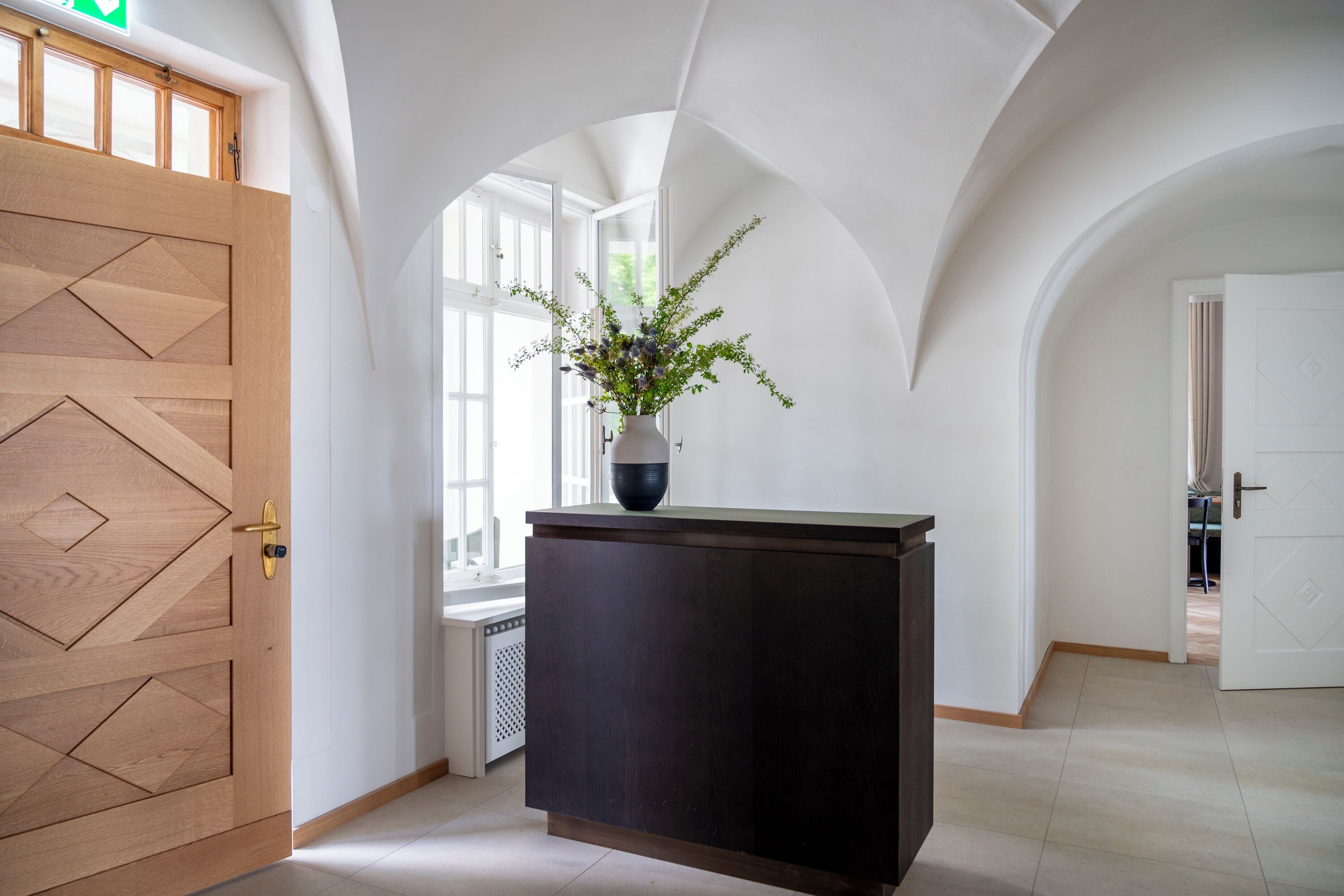 Un'area reception con una porta in legno, una scrivania scura e un vaso con piante.