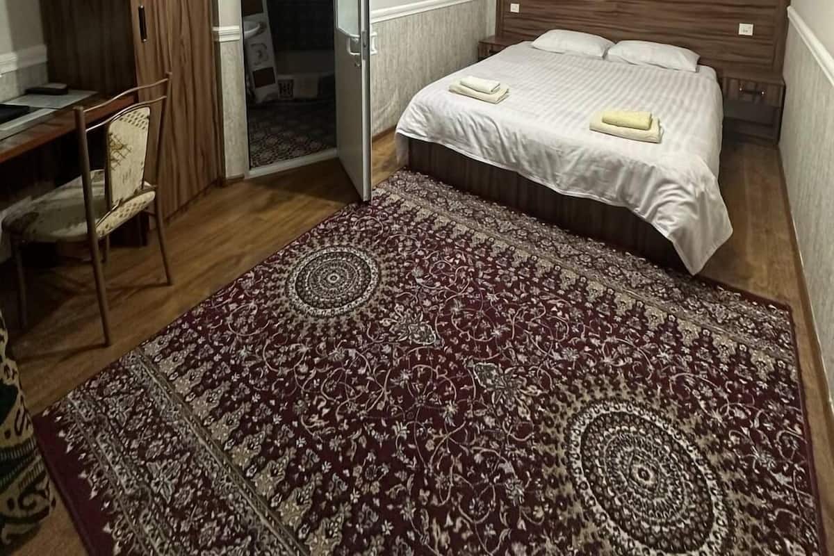 A bedroom with a bed, a desk, a wardrobe, and a door leading to a bathroom.