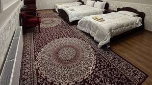 Una habitación de hotel con dos camas, una silla roja, un tapete estampado y un cuadro en la pared.