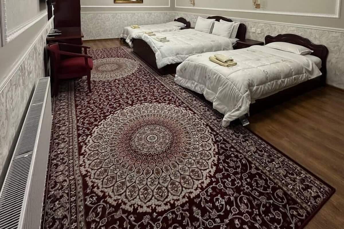 A hotel room with two beds, a red chair, a patterned rug, and a painting on the wall.