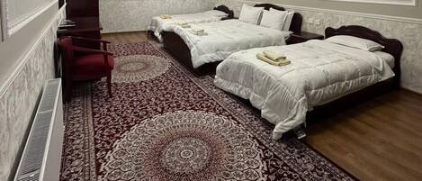 A hotel room with two beds, a red chair, a patterned rug, and a painting on the wall.