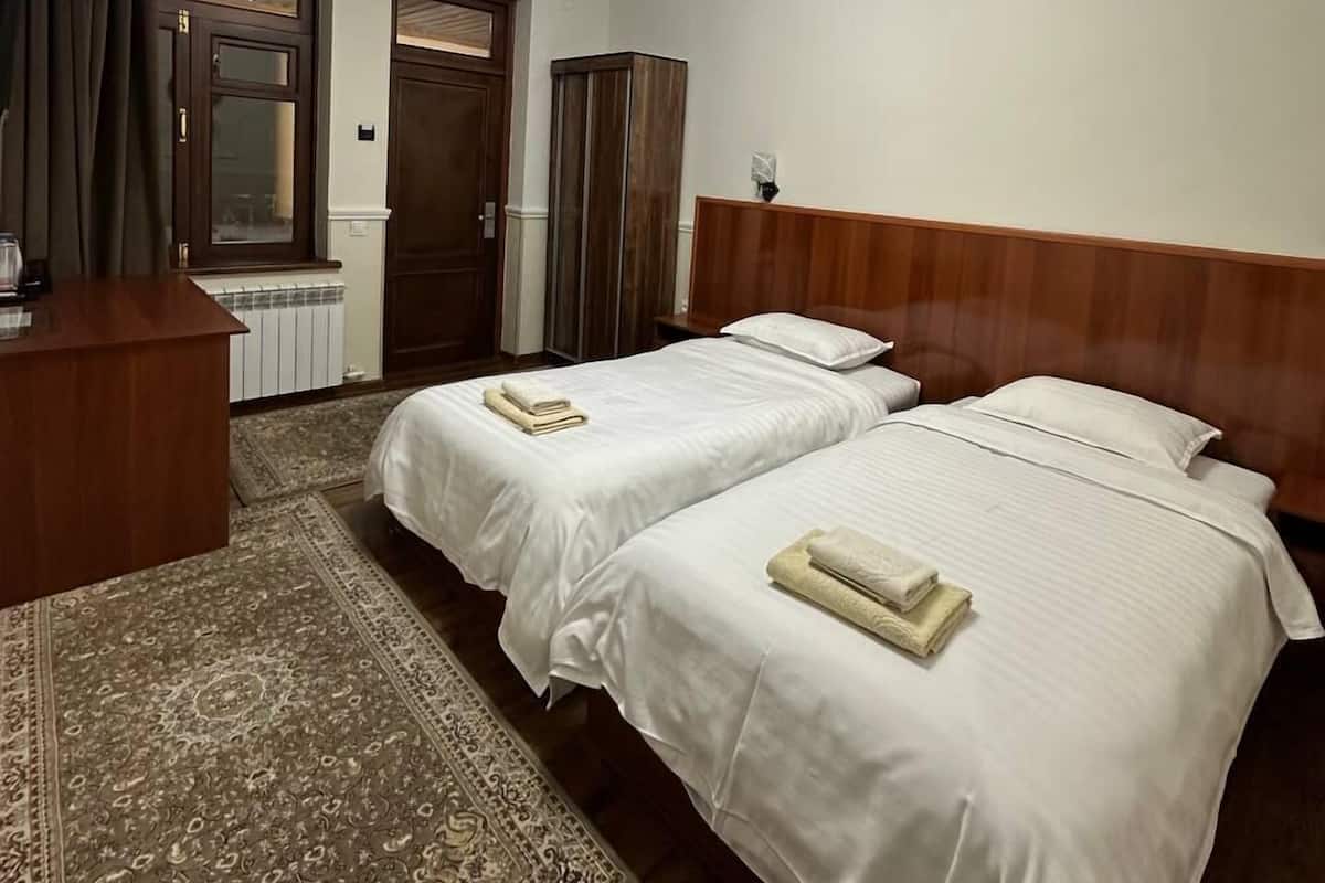 A hotel room with two beds, a wooden headboard, a desk, a mirror, and a patterned rug.