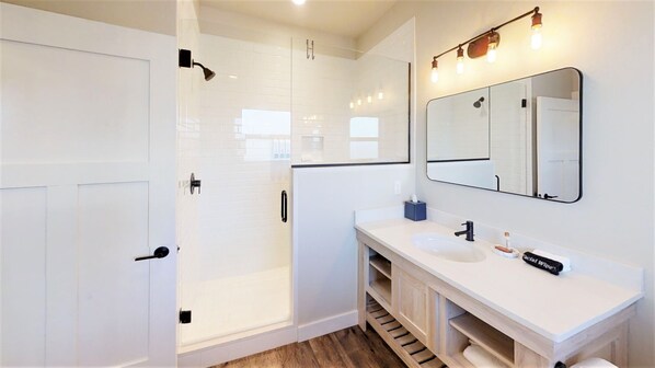 Une salle de bain moderne dotée d’une douche à l’italienne, d’un grand miroir et d’un meuble-lavabo avec un évier et un porte-serviettes.