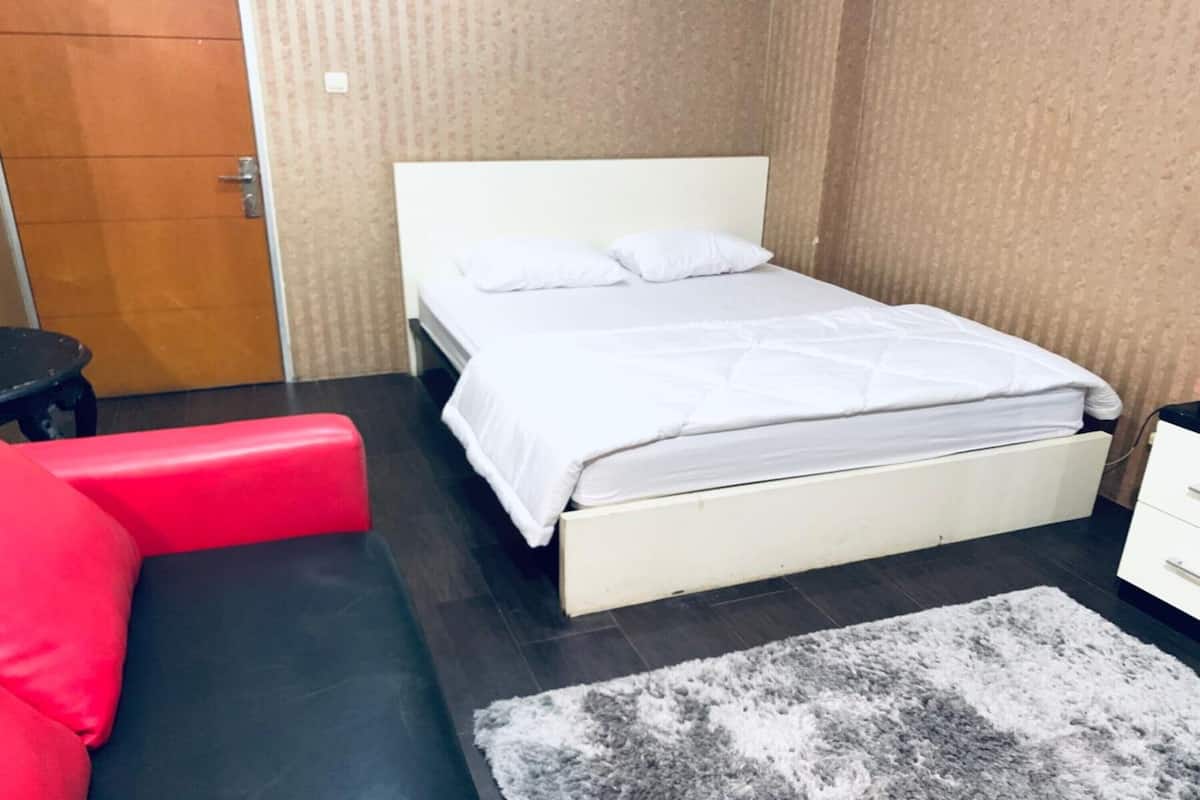 A room with a white bed, a red chair, and a grey rug.
