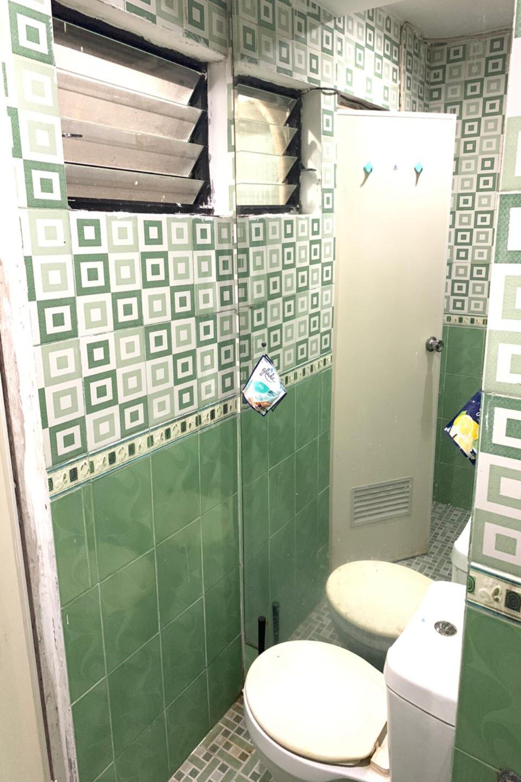 A bathroom with green patterned tiles, a toilet, and a shower area.