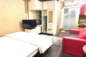 A hotel room with a bed, a TV, a red chair, a wardrobe, and a small kitchenette. - OYO 93585 Apartemen Cibubur Village By Raja Property (Depok)