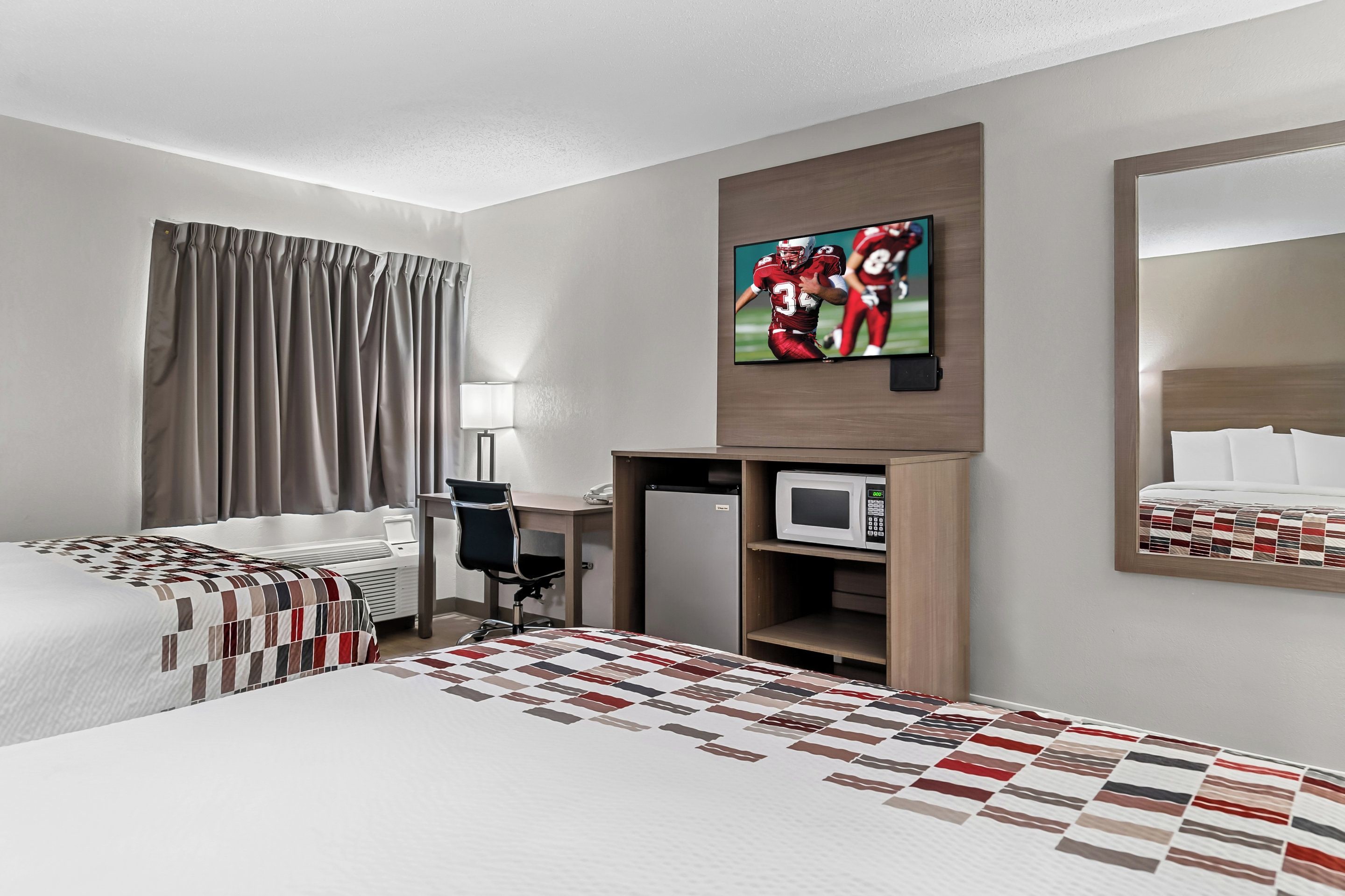 Une chambre d’hôtel avec deux lits, un bureau, un four à micro-ondes et un téléviseur diffusant un match de football.