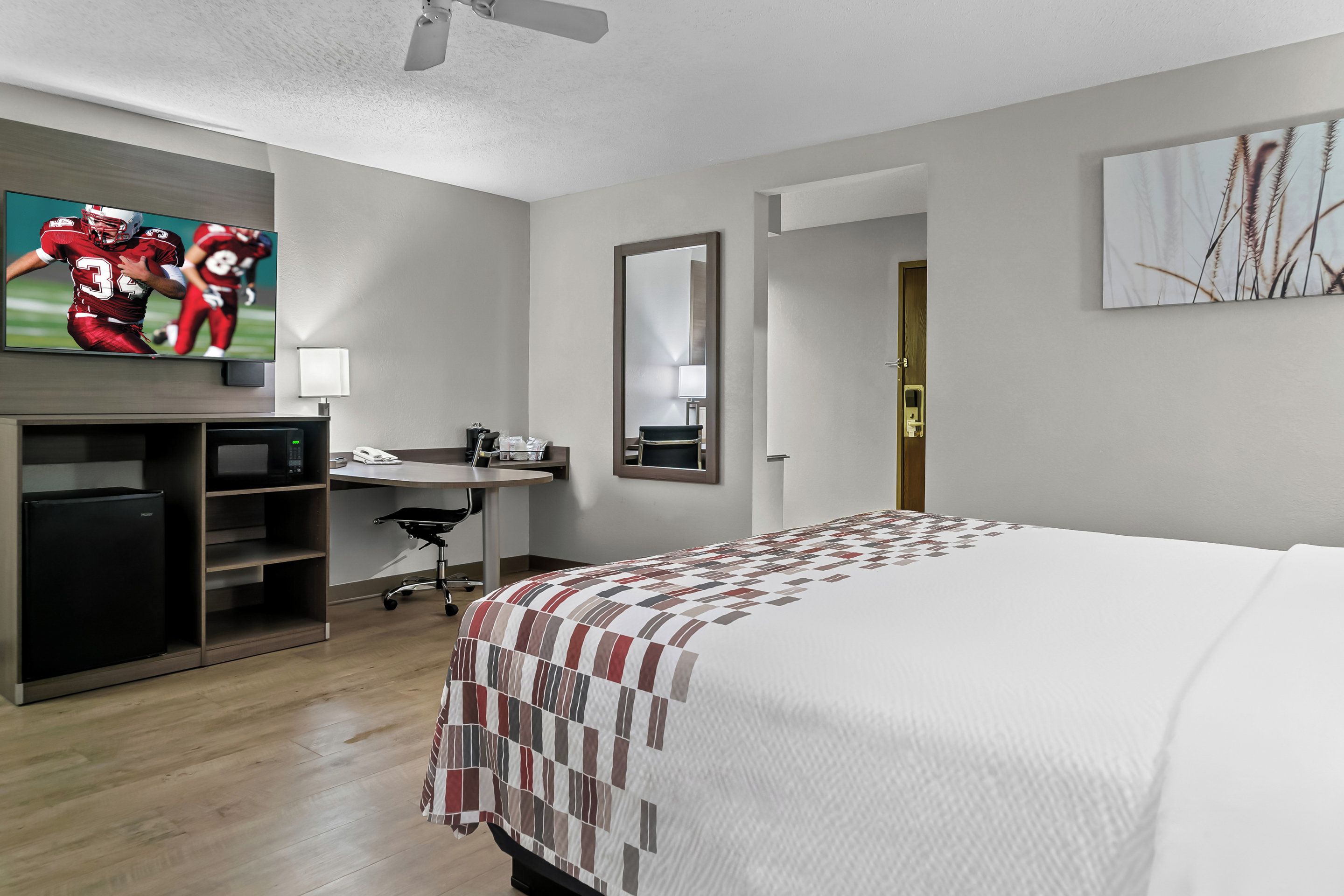 A hotel room with a bed, a desk, a TV, and a mirror.