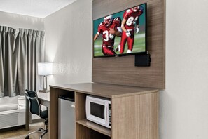 A hotel room with a flat-screen TV mounted on the wall, a desk with a microwave, a chair, and a window with curtains. - Red Roof Inn Flint (Flint)
