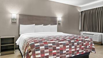 A hotel room with a large bed, two bedside tables, a wall-mounted light, and a window with curtains.