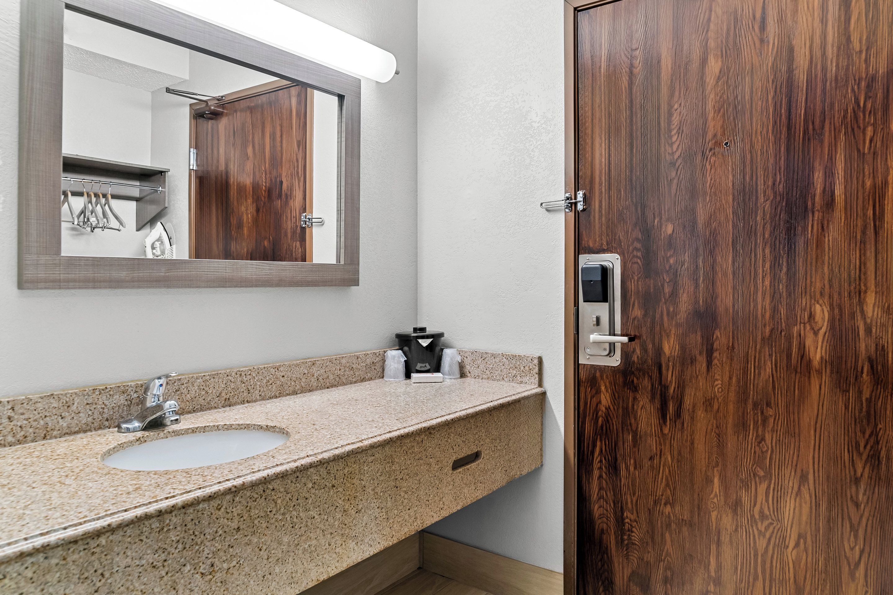 Un baño con lavamanos de encimera de granito, un espejo, una puerta de madera y un perchero para toallas.