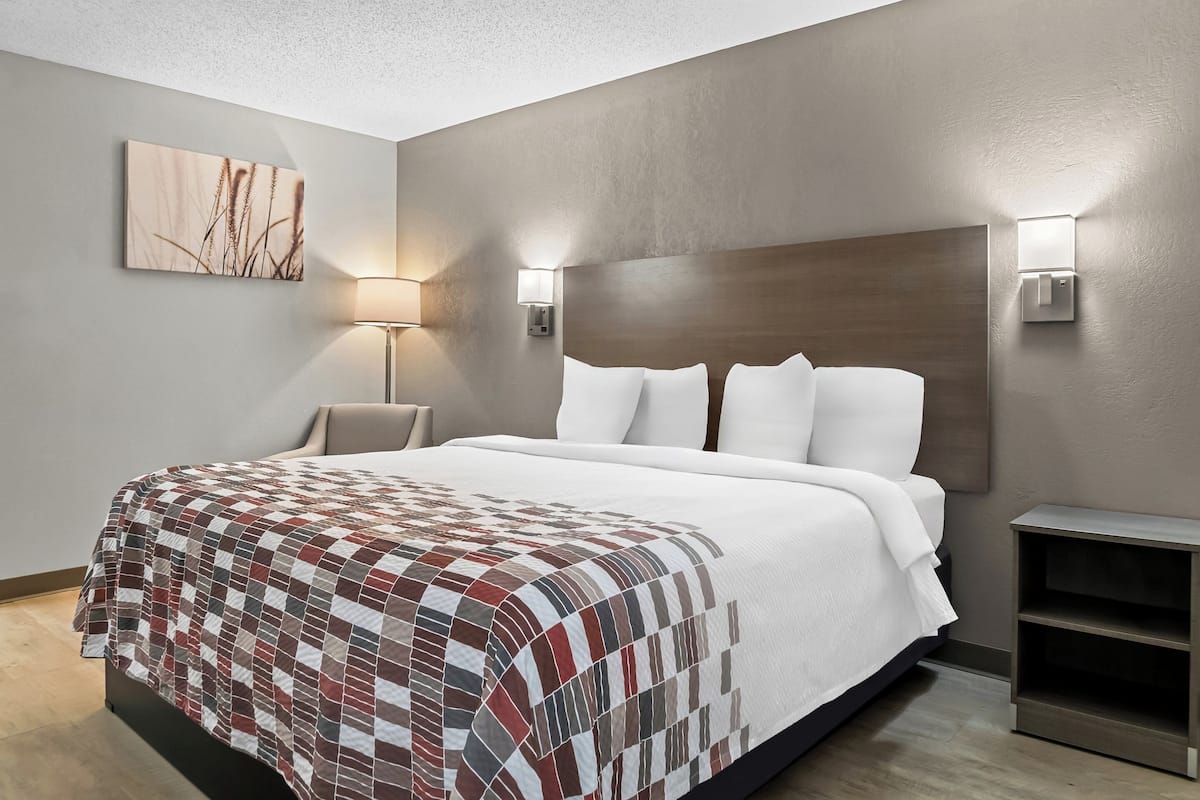 A modern hotel room with a large bed, a headboard, two wall-mounted lamps, a bedside table, and a small nightstand.