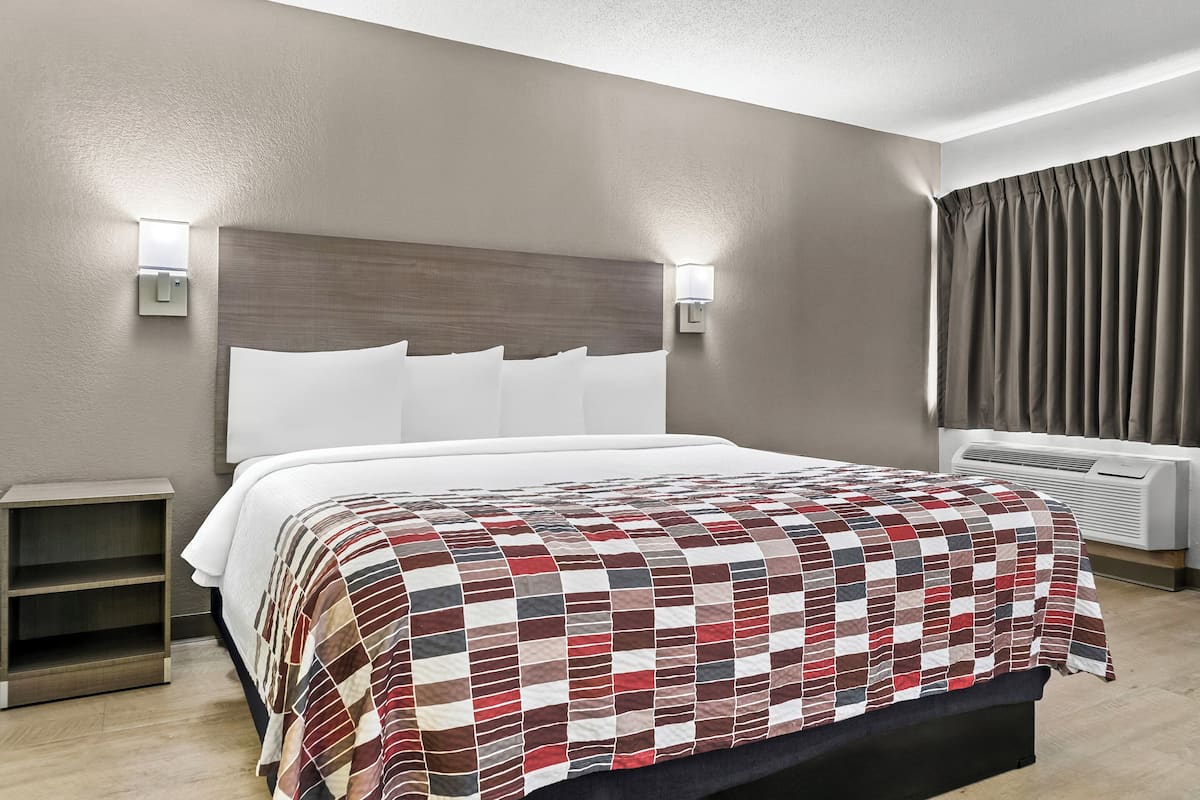 A hotel room with a large bed, two bedside tables, a wall-mounted light, and a window with curtains.