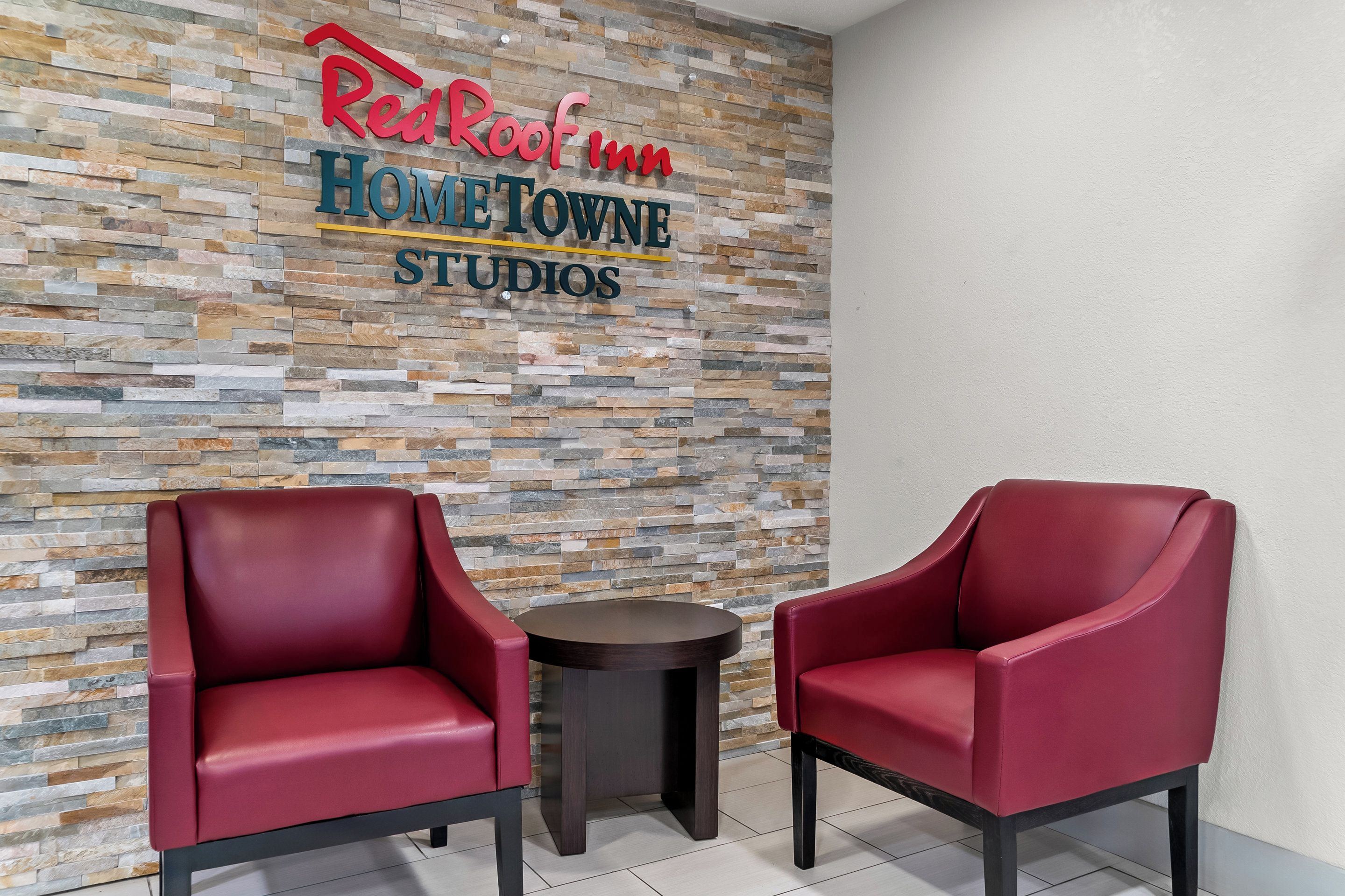 A Red Roof Inn sign on a textured wall, two red chairs, and a small round table.