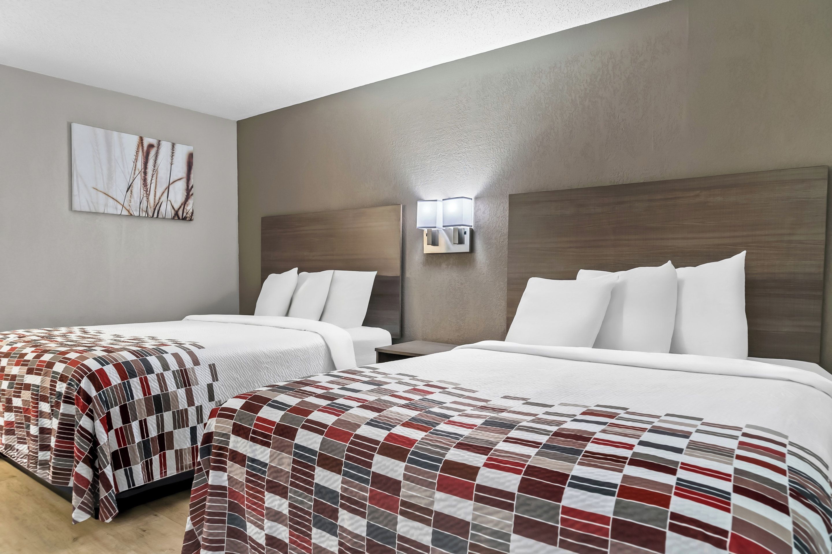 A hotel room with two beds, a large window, and a wall-mounted light fixture.