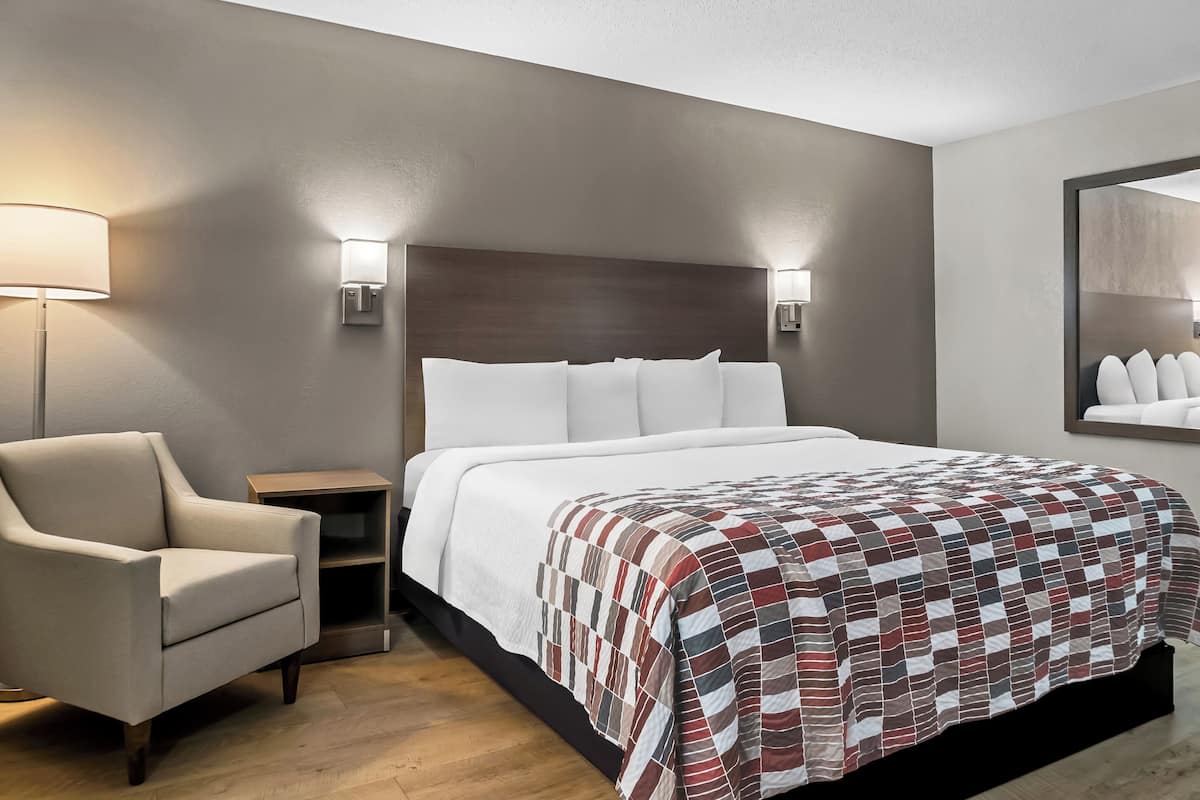 A hotel room with a bed, a chair, a nightstand, and wall-mounted lamps.