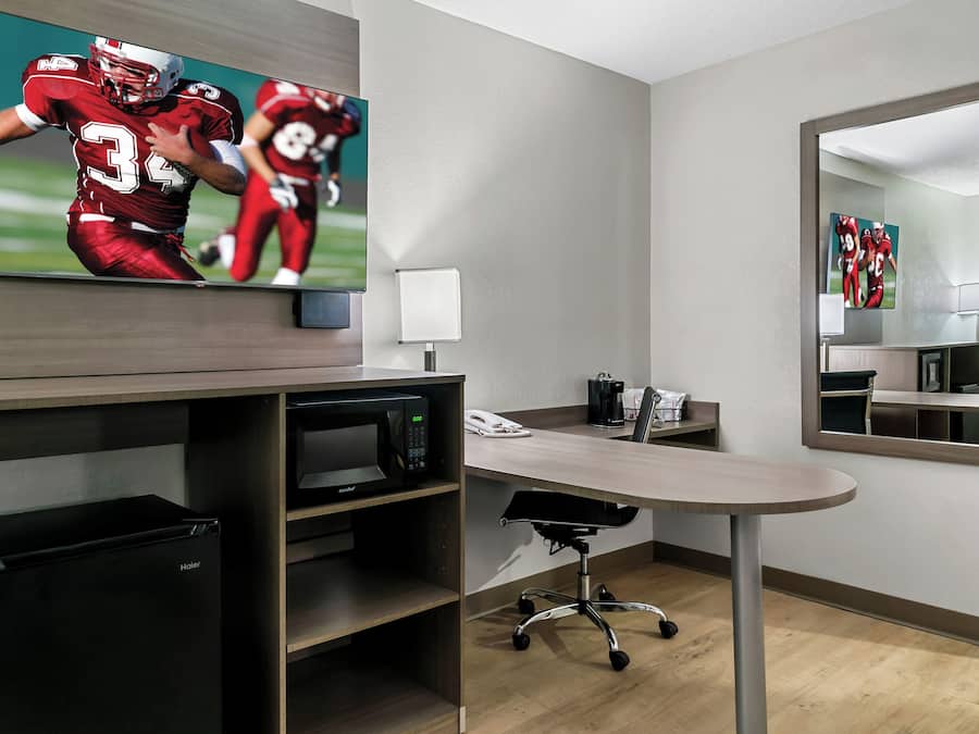 A modern hotel room with a flat-screen TV, a desk with a chair, a microwave, and a coffee maker.