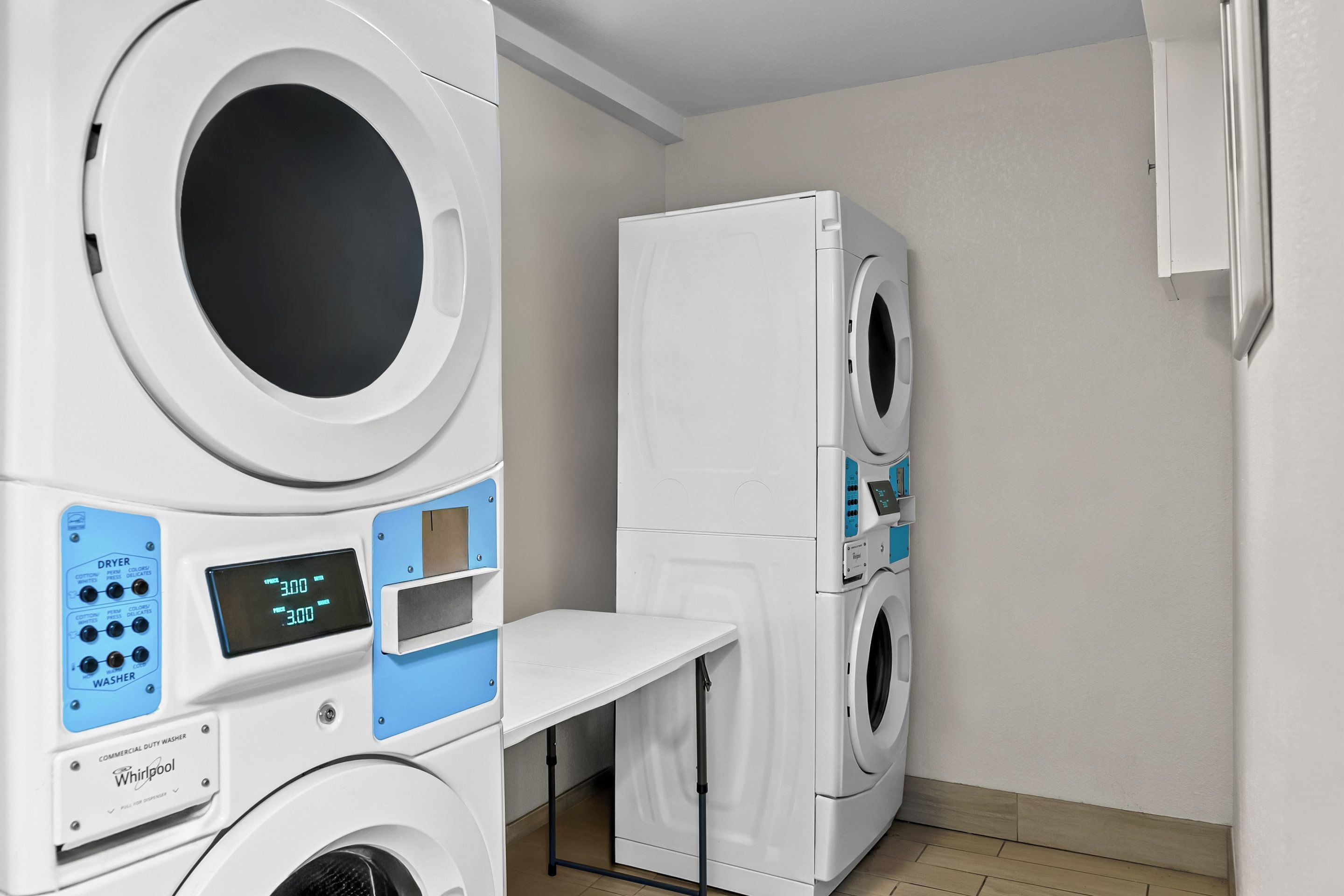 A laundry room with stacked washers and dryers, a control panel, and a small table.