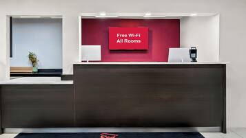 A hotel reception desk with a red wall and a sign stating "Free Wi-Fi All Rooms."