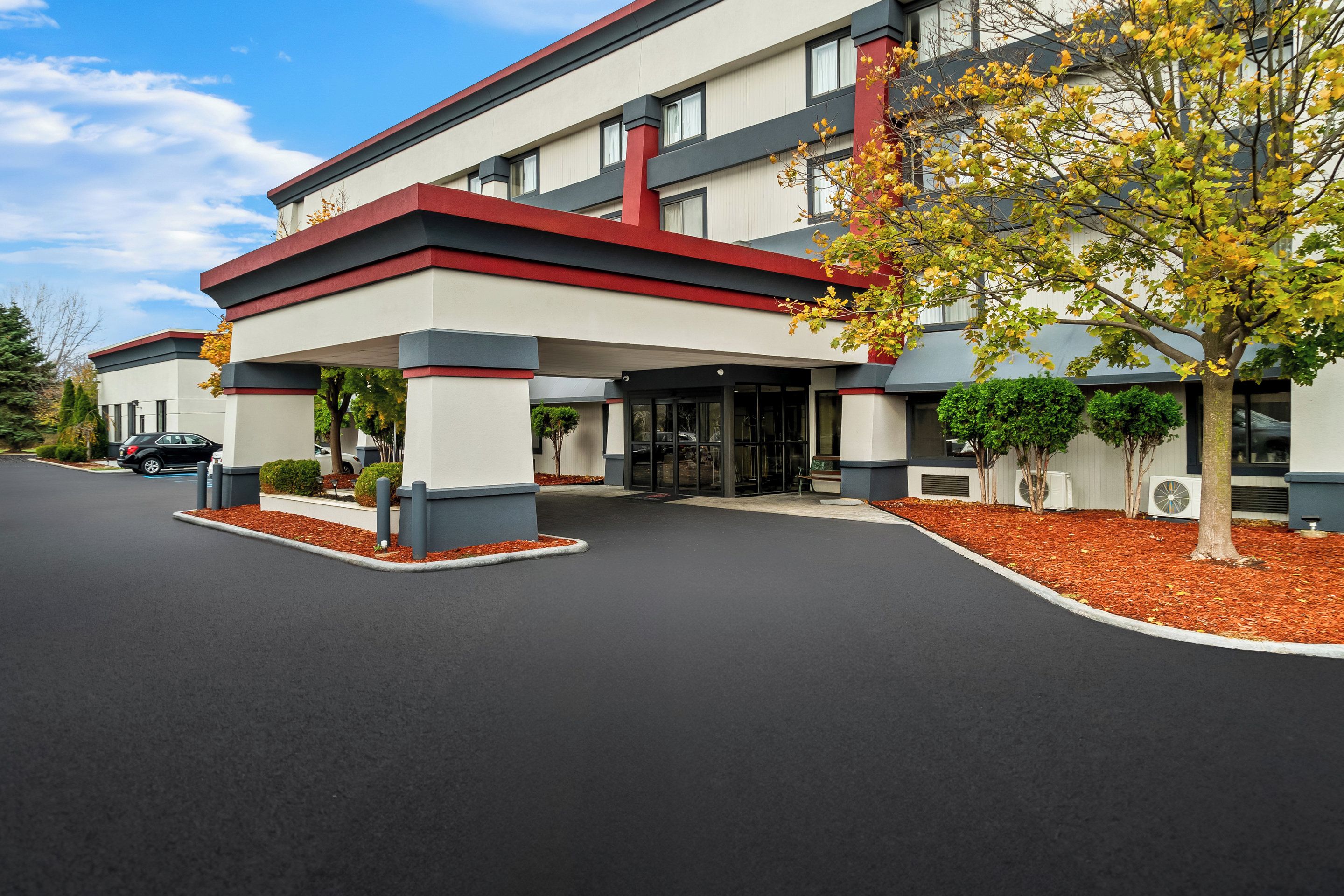 Ein modernes Hotel mit roter und weißer Fassade, überdachtem Parkplatz und einer angelegten Eingangspforte.