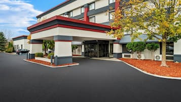 Ein modernes Hotel mit roter und weißer Fassade, überdachtem Parkplatz und einer angelegten Eingangspforte.