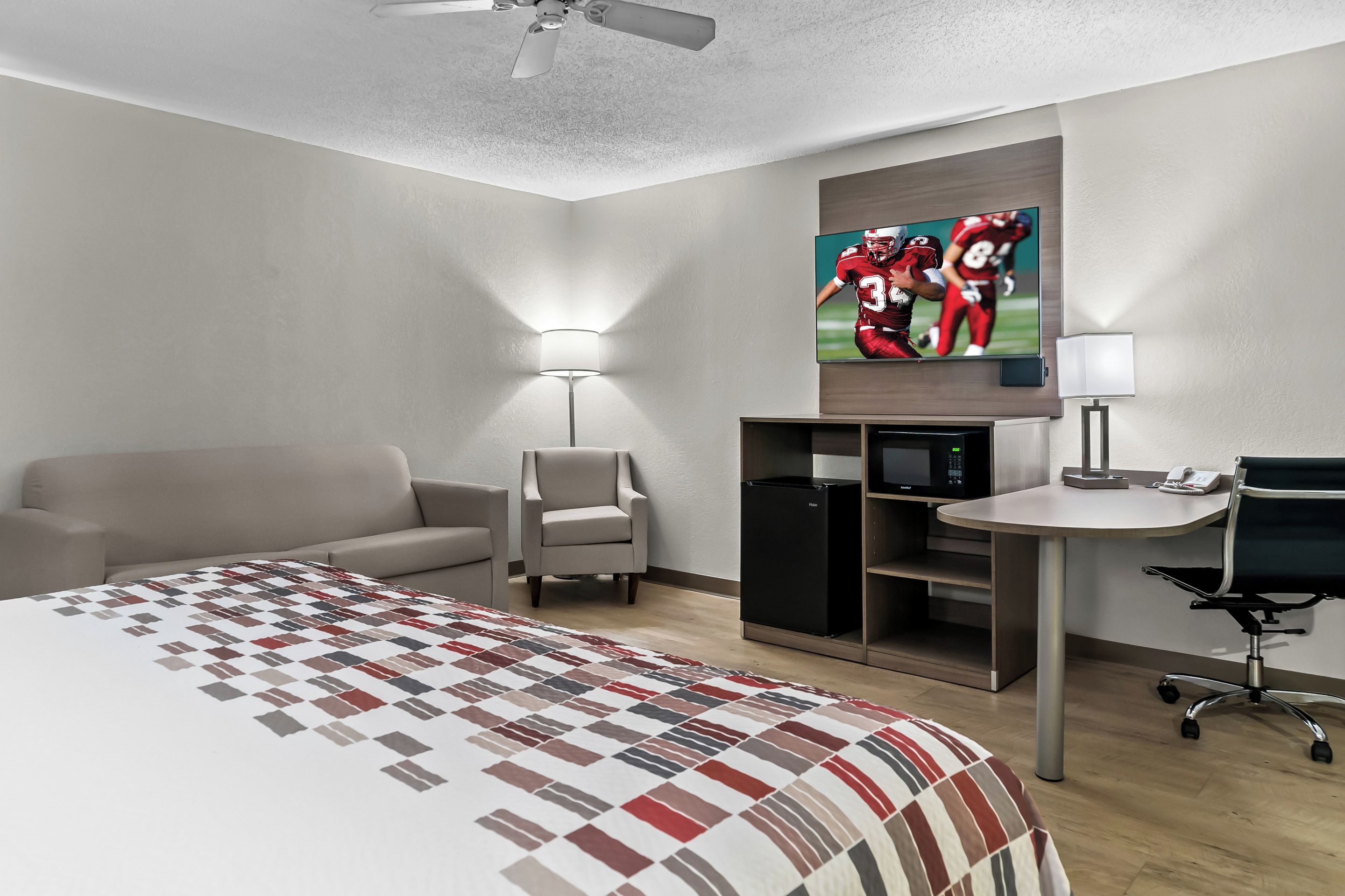 A hotel room with a bed, a desk, a chair, a lamp, a TV, and a wardrobe.