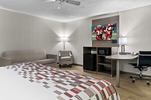 A hotel room with a bed, a desk, a chair, a lamp, a TV, and a wardrobe.