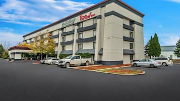 A hotel with a modern design, featuring a Red Roof Inn sign, a parking lot with several cars, and a well-maintained landscaping area.