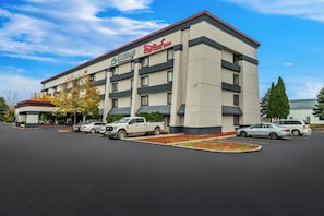 A hotel with a modern design, featuring a Red Roof Inn sign, a parking lot with several cars, and a well-maintained landscaping area. - Red Roof Inn Flint (Flint)