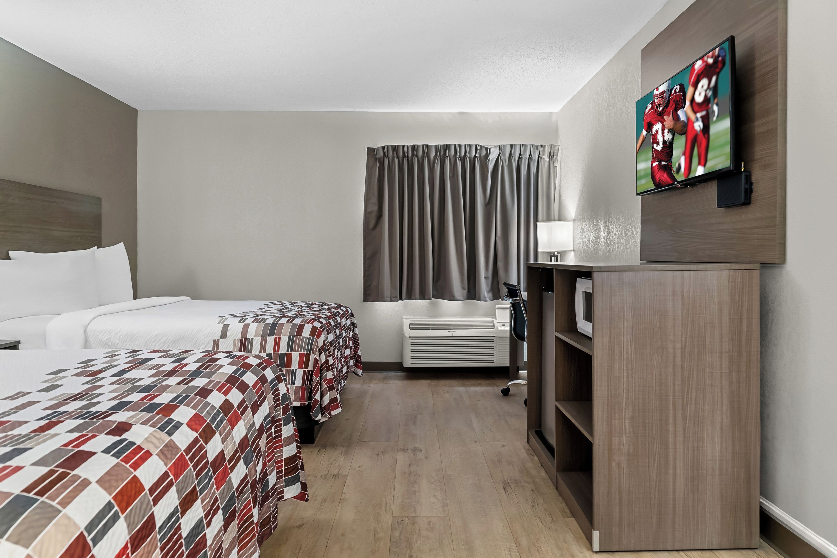 A hotel room with two beds, a flat-screen TV, a desk with a lamp, and a wardrobe.