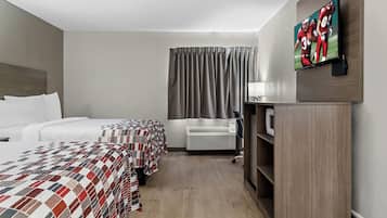 A hotel room with two beds, a flat-screen TV, a desk with a lamp, and a wardrobe.
