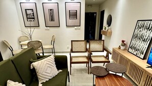 Uma sala de estar moderna com um sofá verde, cadeiras de vime, uma mesa de centro de madeira e quadros nas paredes.