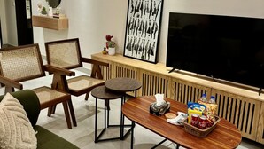 Uma sala de estar moderna com sofá, cadeiras, mesa de centro, televisão e uma moldura na parede.