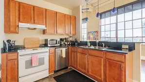 A kitchen with wooden cabinets, a stove, microwave, and a large window with blue pendant lights. - Luxurious Downtown Condo w/ Panoramic City Views and Free Secure Onsite Parking. (New Orleans)