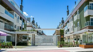 A modern apartment building with a gated entrance, outdoor seating area, and a visible restaurant sign. - WI-FI 300MB | partial view of the SEA #CAMP09 (Florianópolis)