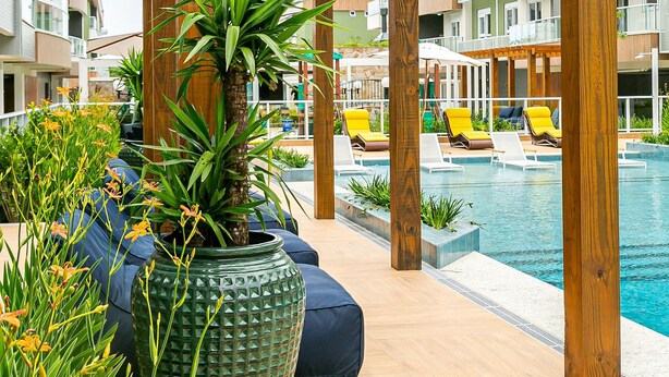 A poolside area with wooden pergolas, lounge chairs, and potted plants. - WI-FI 300MB | partial view of the SEA #CAMP09 (Florianópolis)