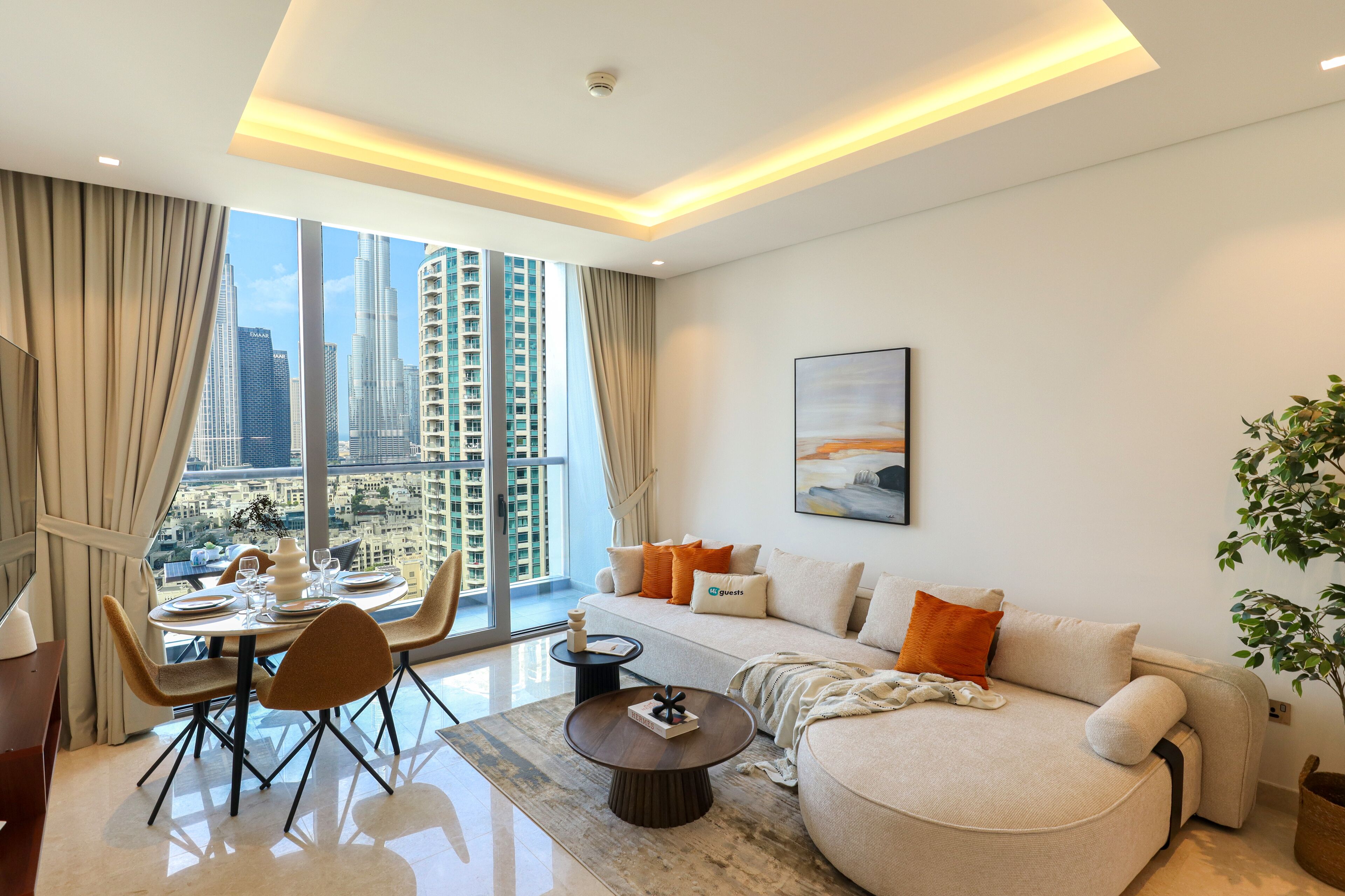 Ein modernes Wohnzimmer mit Essbereich, großen Fenstern und Blick auf die Stadt, einer Couch mit orangefarbenen Kissen und einem Gemälde an der Wand.