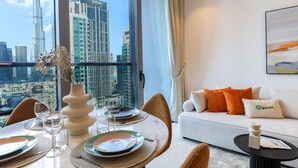 Une chambre d’hôtel moderne dotée d’un coin repas, d’un canapé avec des coussins orange et d’une grande fenêtre donnant sur la ville.