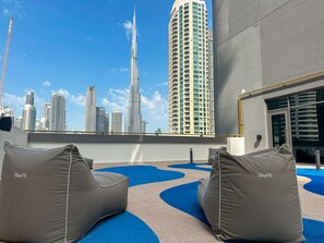Une terrasse sur le toit, agrémentée de deux fauteuils de relaxation Talenti, offrant une vue sur le paysage urbain de Dubaï, notamment sur le Burj Khalifa, et présentant une façade de bâtiment moderne.