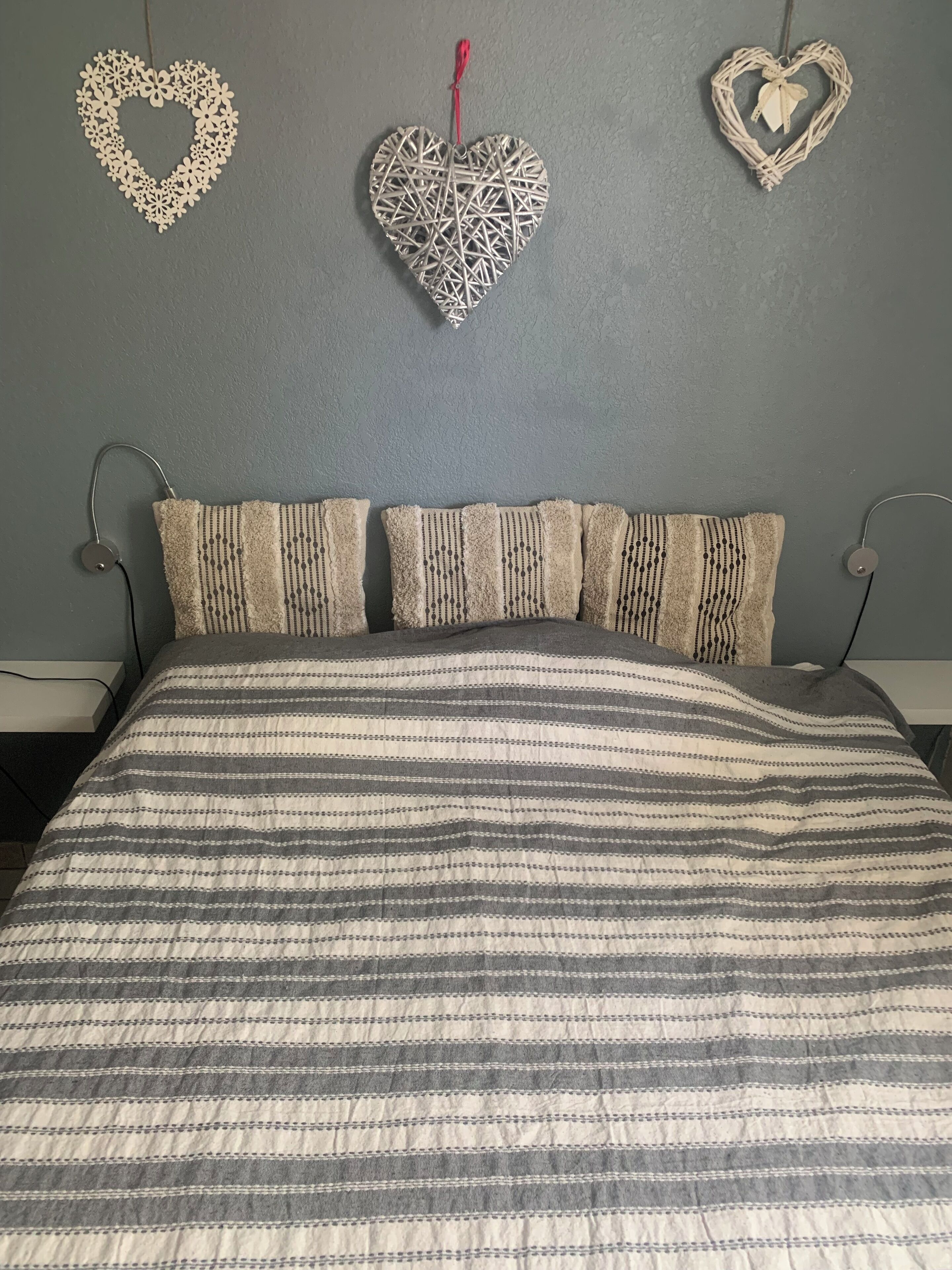 A bed with striped bedding, a grey wall, and two heart-shaped wall decorations.