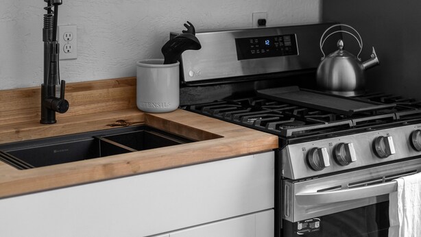A modern kitchen with a wooden countertop, stainless steel appliances, and a kettle. - Lawless Rico: Engel Room (Rico)