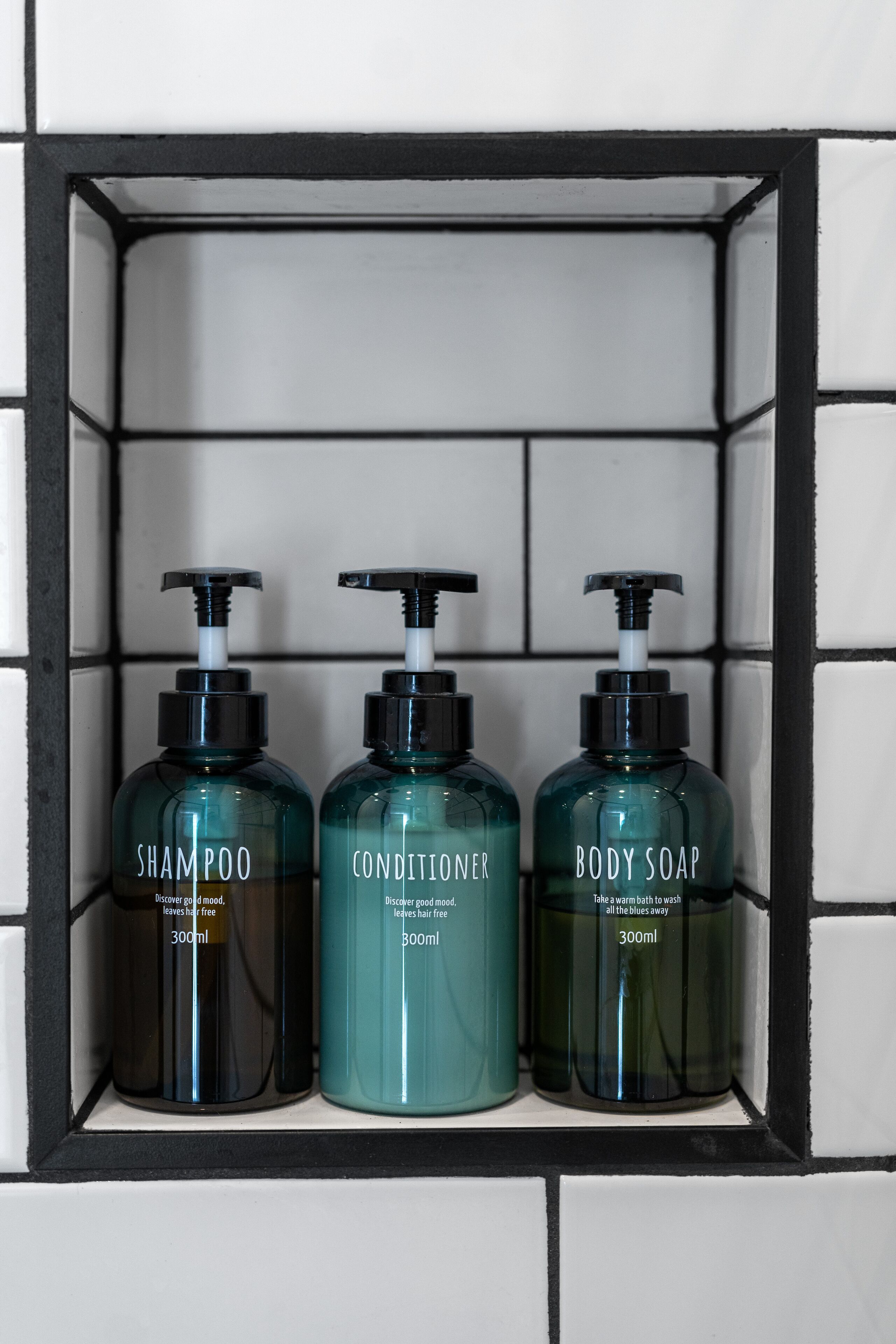 A shelf with three bottles of shampoo, conditioner, and body soap.
